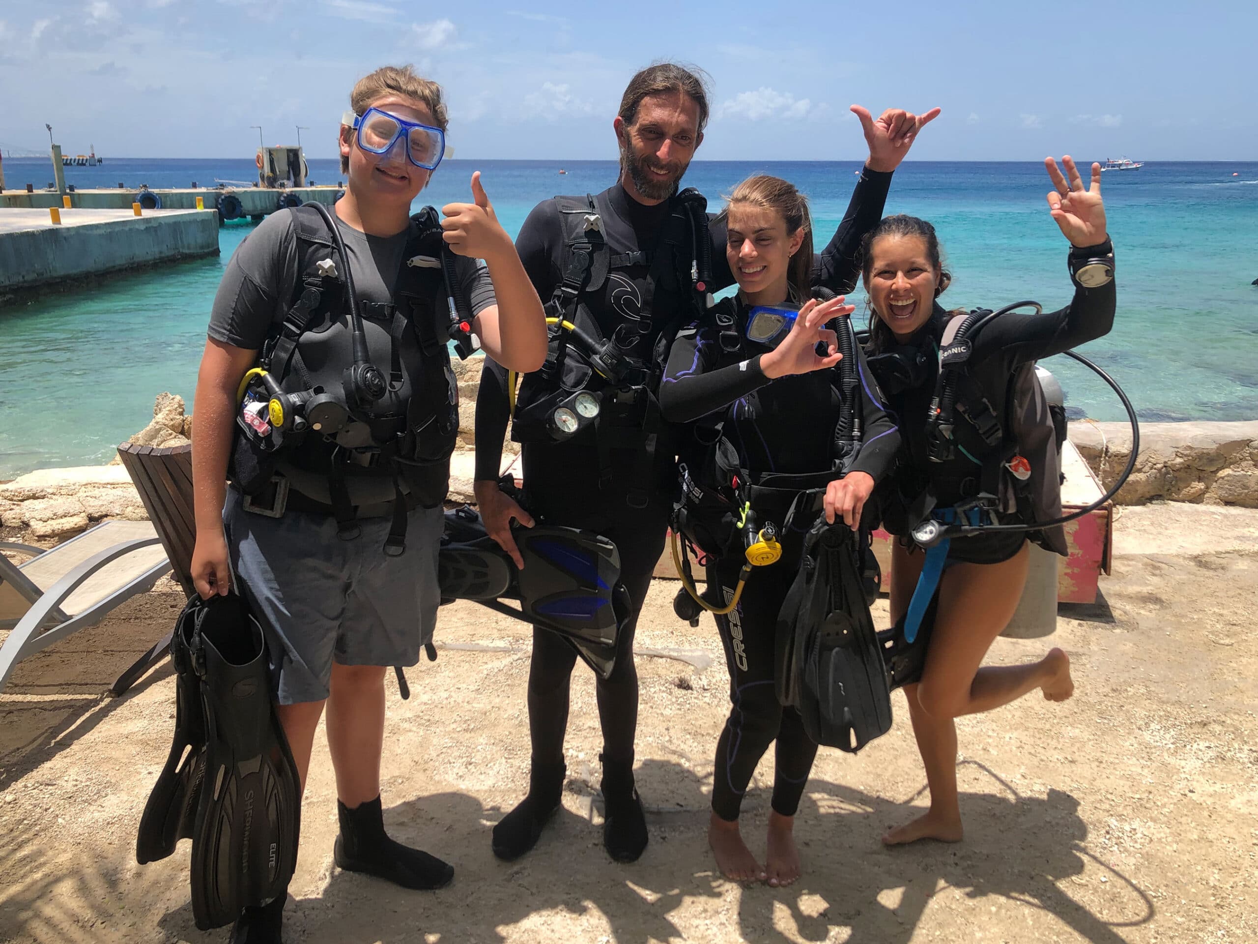 3 Intro Divers & Instructor standing on the beach after a day of diving.