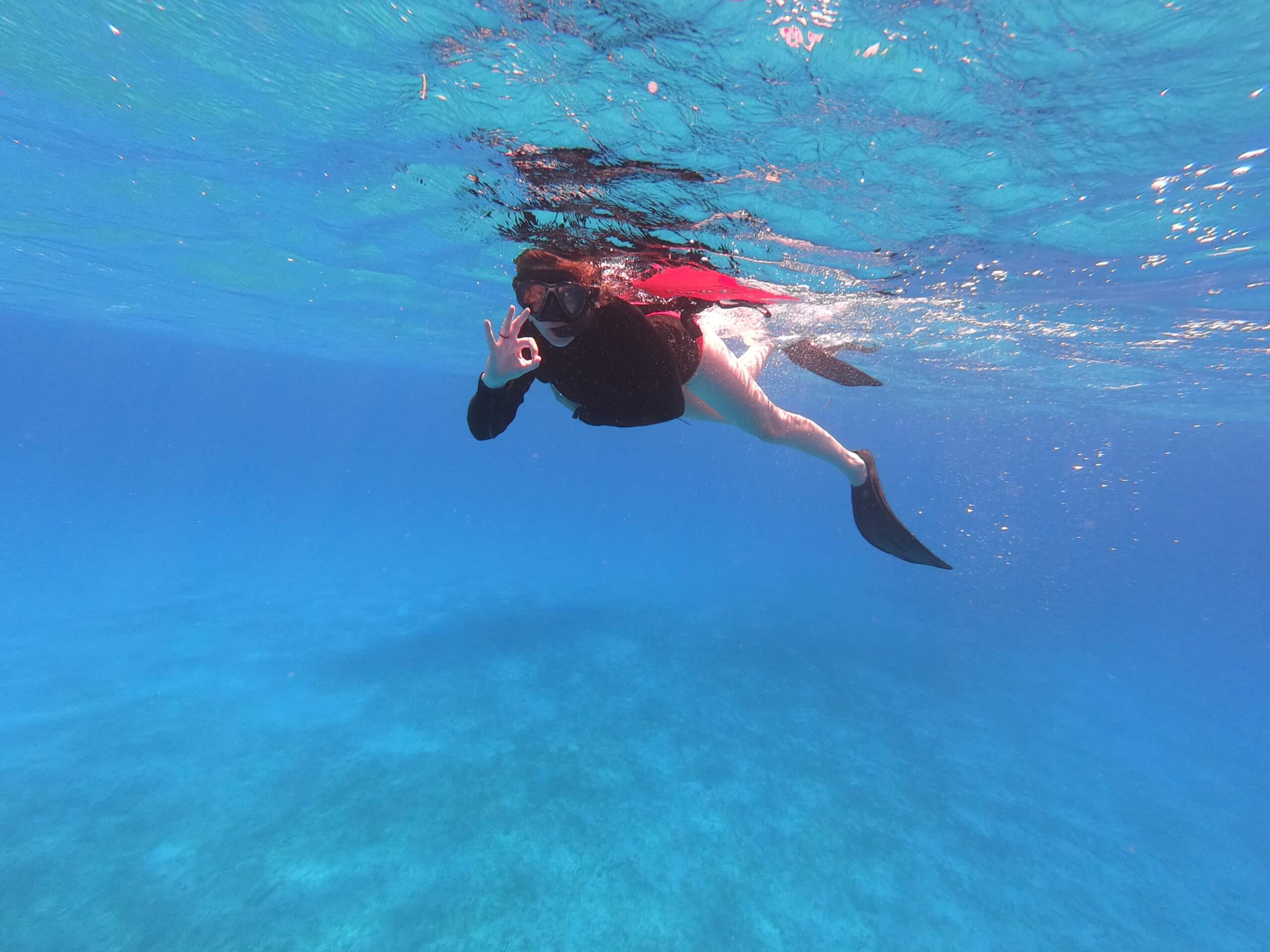 Below-surface photo of a happy snorkeler exploring the shallow sea, signaling ok.